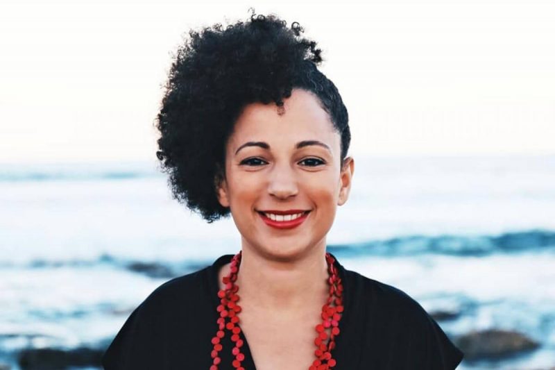 Kizzy Gardiner smiling while standing in front of a lapping shoreline